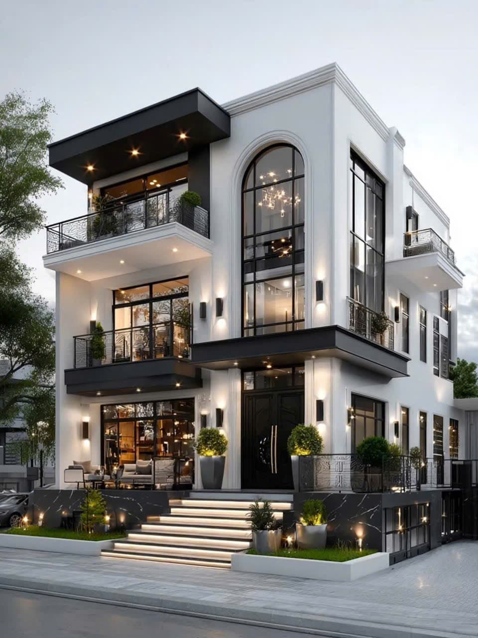 Nhà phố mặt tiền trắng bốn tầng, cửa kính vòm khung đen, ban công và bậc thềm đá sáng đèn buổi tối.